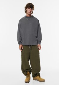 Sweatshirt gris surdimensionné avec un col rond, associé à un pantalon cargo vert olive avec des poches latérales, et des bottes brunes à lacets.