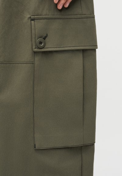 Jupe cargo vert olive avec une grande poche avant à fermeture bouton, coutures plates et texture lisse. Coupe ajustée qui souligne la silhouette.