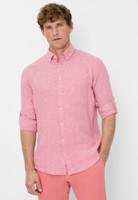 Camicetta button-up rosa chiaro con un motivo testurizzato, maniche arrotolate, piccola tasca sul petto e tessuto leggero, abbinata a pantaloni rosa.