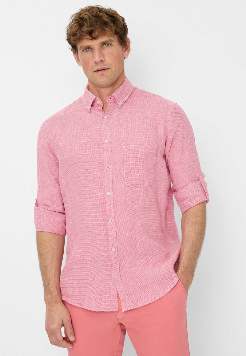 Camicetta button-up rosa chiaro con un motivo testurizzato, maniche arrotolate, piccola tasca sul petto e tessuto leggero, abbinata a pantaloni rosa.