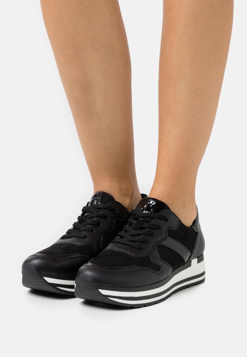 Baskets de sport noires en matériaux en maille et synthétiques, à bout rond, avec des accents texturés et des rayures blanches contrastantes sur la semelle.