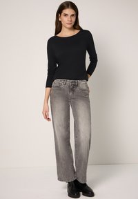 Schwarzes langärmliges Oberteil mit U-Boot-Ausschnitt; graue Jeans mit weitem Bein und verblasstem Finish; kombiniert mit schwarzen Stiefeletten; minimalistischer Stil.