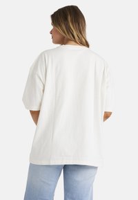 Oversized hvid T-shirt lavet af blødt bomuld, med rund halsudskæring og korte ærmer, båret med lyseblå jeans, som fremhæver en afslappet pasform.