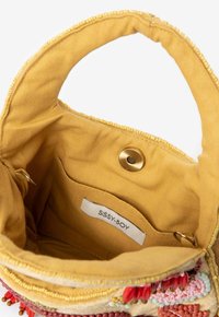 Intérieur d'un sac à main en tissu jaune, avec une texture lisse, une fermeture à pression magnétique et une petite poche avec une étiquette. Perles décoratives à l'ouverture.