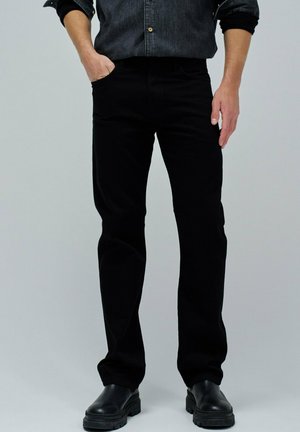 Jeans de mezclilla negra con corte slim, que cuentan con bolsillos frontales y una cinturilla clásica. Combinados con una camisa oscura y botas de tobillo negras.