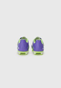 Scarpini da calcio viola con accenti verdi, dotati di una superficie testurizzata e tacchetti sagomati per una migliore trazione. La vista posteriore mostra i motivi di design e il logo.