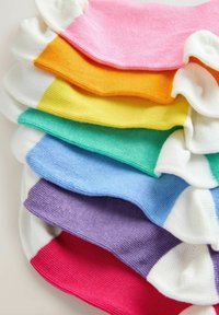 Calcetines de algodón coloridos apilados en capas verticales: rosa, naranja, amarillo, verde, turquesa, azul, púrpura y rojo. Cada uno con secciones de punta blanca en contraste.