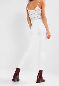 Jeans skinny blancos de cintura alta, combinados con una blusa floral clara y botines de tacón burdeos. Textura suave y diseño ajustado.