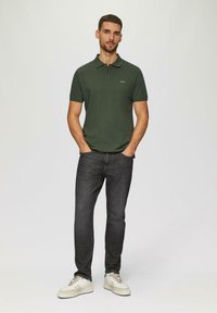 Ciemnozielona koszulka polo, slim-fit dżinsy, białe sneakersy. Posiada kołnierz i małe logo na piersi. Gładka faktura, casualowy design.