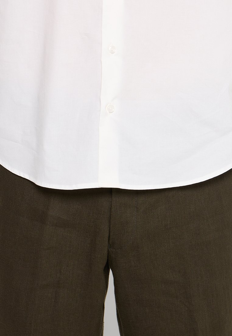 Witte button-down shirt met een gladde textuur en een ronde zoom, gecombineerd met donkerbruine linnen broeken met een licht gestructureerd oppervlak.