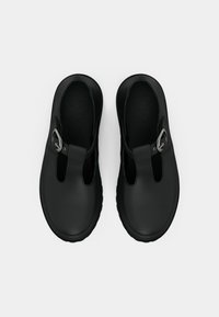 Μαύρα ελαστικά παπούτσια με σχέδιο T-bar, λεία υφή και ασημένια λεπτομέρεια στο κούμπωμα. Στρογγυλή μύτη και επίπεδη σόλα.