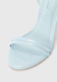 Sandalia de tacón alto vegana de color azul claro con un acabado brillante, tiras estrechas y un diseño de punta afilada para una silueta elegante.