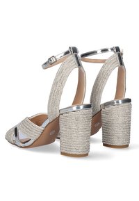 Sandalias de tacón alto glamorosas con un acabado metálico plateado, correas de tela texturizada y acentos brillantes en un tacón ancho.