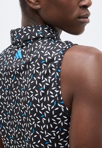 Κοντινό πλάνο ατόμου που φοράει μαύρο αμάνικο τοπ με λευκά και μπλε σχέδια που μοιάζουν με φύλλα και μπλε λογότυπο στον γιακά στην πλάτη.