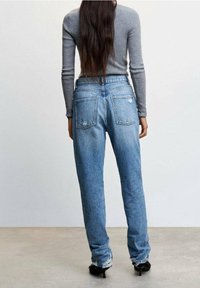 Jean bleu clair déchiré avec une coupe décontractée, comprenant deux poches arrière, des ourlets effilochés et une taille mi-haute.