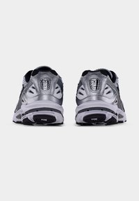 Harmaat ja mustat urheilukengät, joissa on verkkokankaasta valmistettu päällinen, heijastavia yksityiskohtia ja kuvioitu pohja, suunniteltu mukavuutta ja tukea varten.