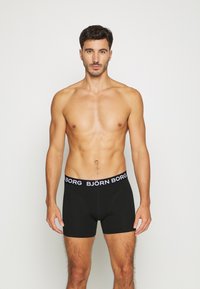 Schwarze Boxer-Briefs mit einem elastischen Bund mit Logo. Der Stoff wirkt glatt und sitzt gut, mit einem schlichten Design ohne Muster.