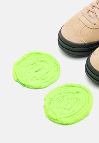 Beige suede sneaker with black rubber sole, positioned near two spiral green terry cloth pads, showcasing their texture and vibrant color.