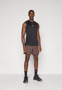 Black sleeveless athletic top with a white logo, brown shorts, black socks, and black athletic shoes with a textured surface and laces.