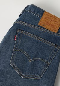Πίσω τσέπη μπλε τζιν Levi's 501 με πορτοκαλί ραφές, κόκκινη ετικέτα Levi's και μπεζ δερμάτινη ετικέτα με μέγεθος W32 L32.