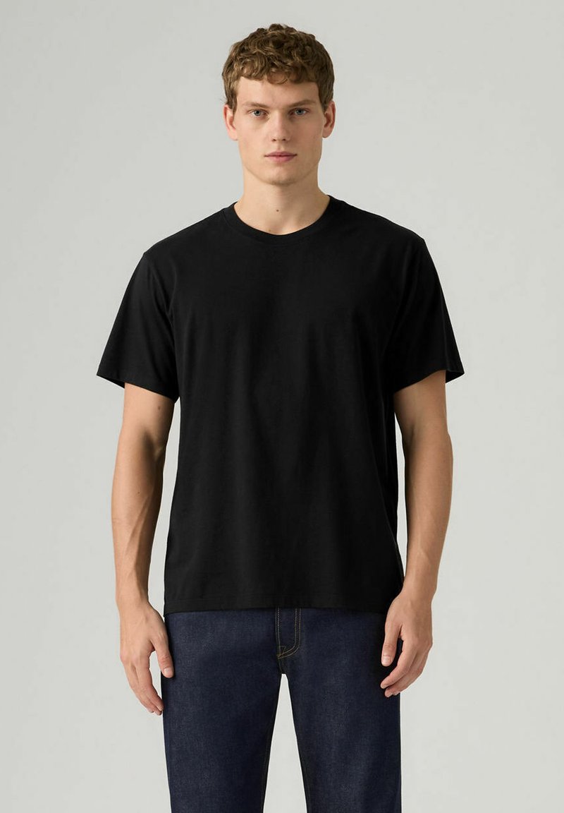 T-shirt nera in cotone con scollo rotondo classico e maniche corte, indossata da una modella su uno sfondo neutro, abbinata a pantaloni in denim.