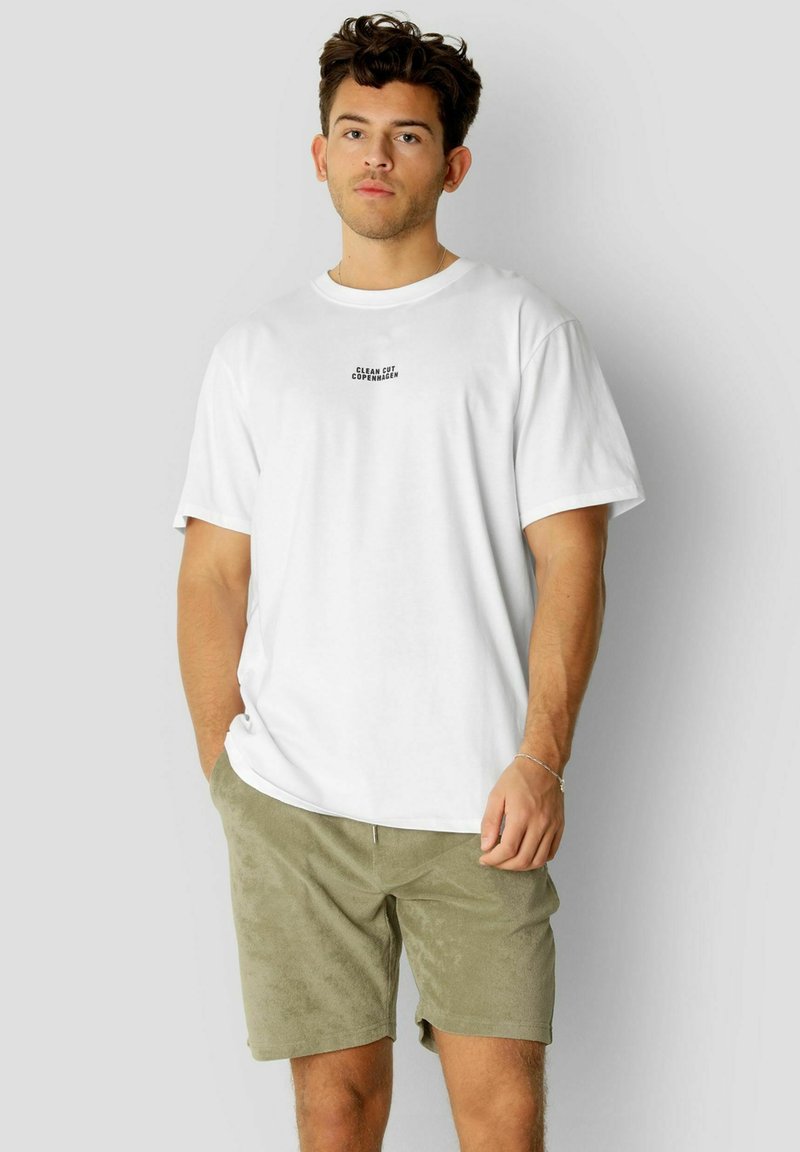Hvit bomull t-skjorte med korte ermer, med svart tekst "CLEAN CUT COPENHAGEN" i sentrum. Kombinert med olivgrønne teksturerte shorts.