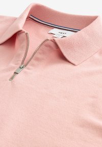 Polo din bumbac roz deschis cu fermoar, având un finisaj texturat, prezentând un guler în dungi contrastante bleumarin și alb. Detalii de design blânde și lejere.