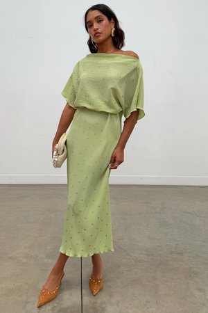 Robe vert clair avec un design décolleté, en tissu texturé et avec des motifs discrets de points dorés. Associée à des escarpins pointus beiges et une pochette crème.