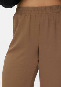 Brązowe, miękkie spodnie z tkaniny z elastycznym paskiem w talii; gładka faktura; zwężany krój bez kieszeni; odpowiednie do noszenia na co dzień.