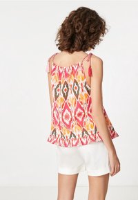 Haut sans manches coloré en motif ikat rose, orange et vert. Présente un ourlet froncé et des bretelles à nouer avec des glands.