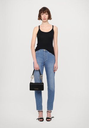 Melnās bez piedurknēm tank tops, augstās vidukļa gaiši zilas bikses un maza melna rokassomiņa ar ķēdes siksniņu, izliktas uz neitrāla fona.