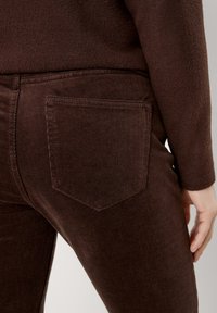 Pantalones de pana marrones con un acabado texturizado y un bolsillo trasero rectangular, ubicado en el lado derecho.