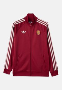 Rød sportjakke med lynlås, hvide Adidas-striber på ærmerne, Adidas-logo på venstre bryst og Spaniens nationalemblem på højre bryst.