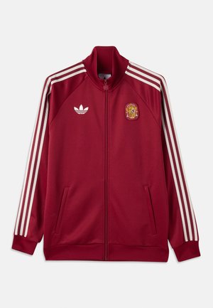 Rød sportsjakke med glidelås og hvite Adidas-striper på ermene, Adidas-logo på venstre bryst og Spaniens nasjonale emblem på høyre bryst.