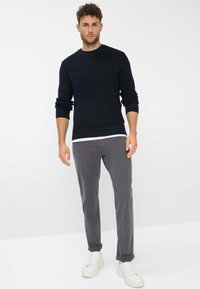 Maglione blu navy a maglia con scollatura a girocollo, abbinato a pantaloni grigi slim-fit e sneakers bianche. Tessuto liscio con dettagli a costine sui polsini.