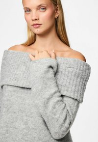 Suéter gris con los hombros al descubierto, puños acanalados y un cuello doblado. Textura de punto suave con un ajuste holgado, que muestra un diseño casual.