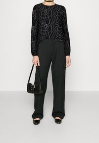 Maglia nera a maniche lunghe con motivo astratto bianco, abbinata a pantaloni cargo neri e scarpe slip-on nere. Piccola borsa nera con dettagli in argento.