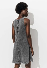 Robe en denim sans manches en lavage noir. Présente un col rond, une fermeture à boutons dans le dos et des coutures visibles le long des coutures.