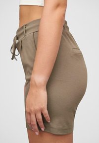Olivové elastické šortky s elastickým pásom a šnúrkou. Majú jednoduchý design, bočnú kapsu a hladkú textúru.