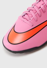 Nærbilde av en rosa treningssko med en lys rød Nike swoosh, teksturerte lisser og en svart såle.