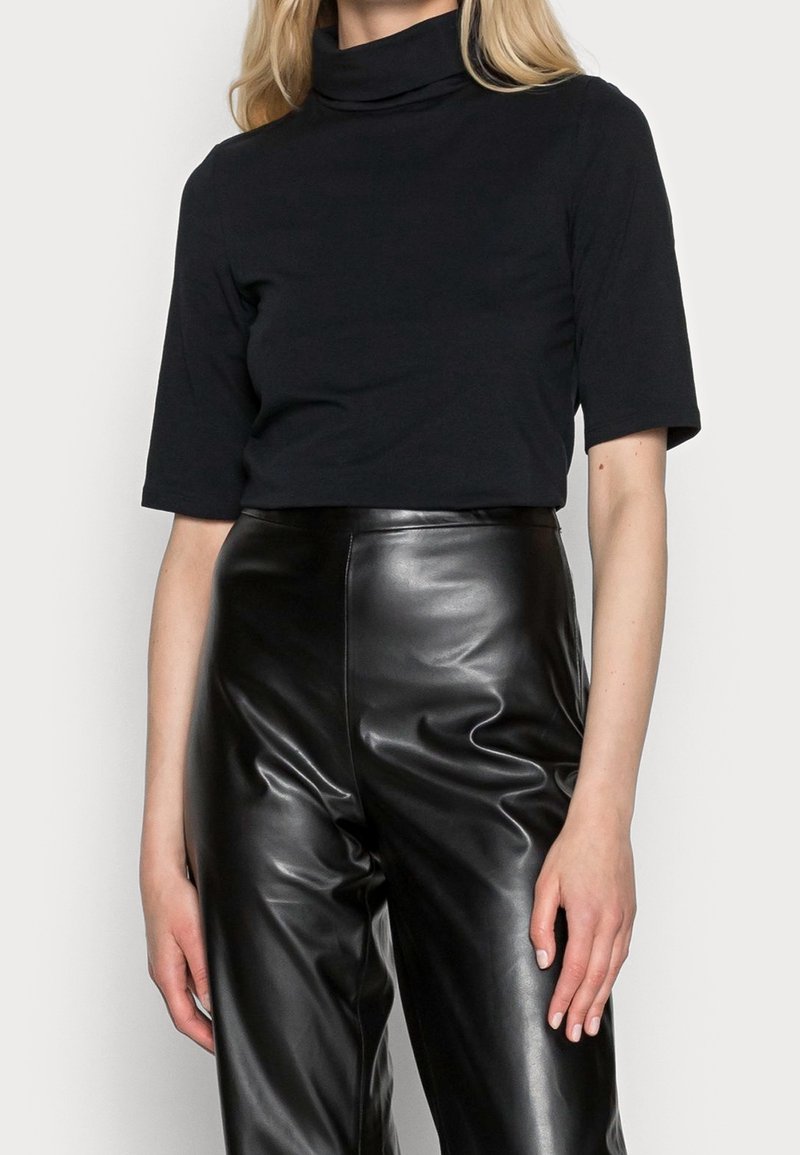 Top negro de manga corta y cuello alto en una tela suave y flexible, combinado con pantalones de imitación cuero negros de cintura alta con un acabado brillante.