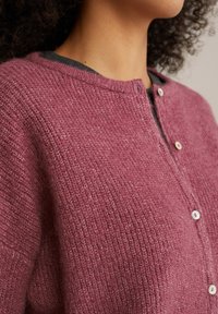 Cardigan v teksturiranem burgundskem pletenju, z okroglim izrezom, zapiranjem na gumb in subtilnim heather vzorcem. Mehko, udobno blago.