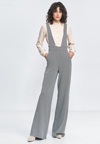 Szerokie ogrodniczki w szare paski z regulowanymi ramiączkami, noszone na jasnoszarej koszuli z guzikami. Gładki materiał o luźnym kroju.