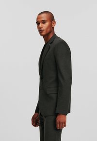 Mörkgrå skräddarsydd kostym med blazer och matchande byxor. Har en stilren design, texturerad tyg och en enkelknappsstängning.