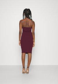 Vinröd axelbandslös klänning, figurnära design, knälång. Mjuk textur, minimal detaljering, matchad med nudefärgade högklackade sandaler.