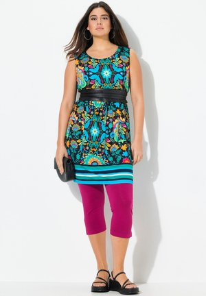 Robe tunique multicolore à fleurs avec ceinture noire, bas turquoise rayé, associée à des leggings capri magenta et des sandales noires.