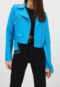 Modrá zkrácená bunda z umělé kůže ve stylu motorkářské bundy se stříbrnými prvky, kapsami na zip a detailem pásku; dlouhé rukávy se zatlačovacími akcenty.