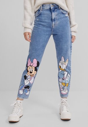 Jeans en denim bleu clair à taille haute, avec des imprimés graphiques colorés de Minnie Mouse et Daisy Duck sur chaque jambe, et des détails usés.
