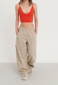 Červený pletený crop top s výstřihem do V, spárovaný s béžovými volnými kalhotami s velkými kapsami a elastickým pasem. Světlé tenisky.