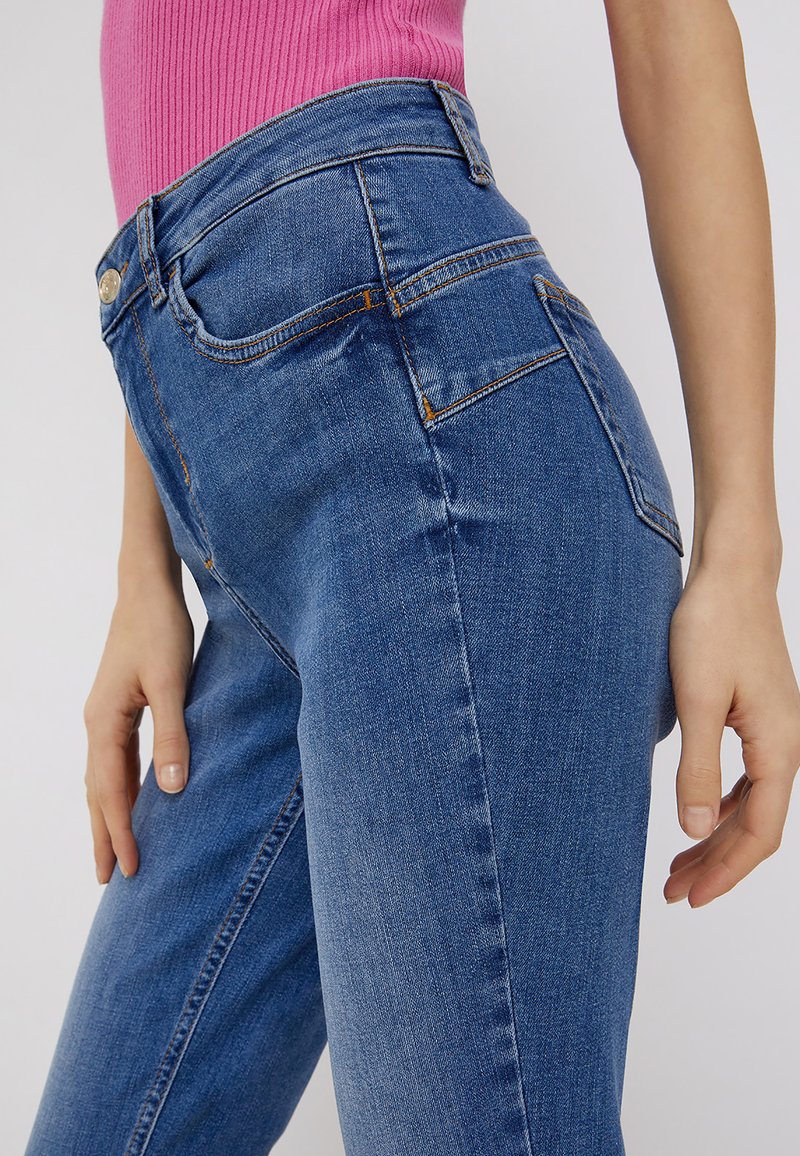 Jeans blue a vita alta realizzati in denim, con un classico design a cinque tasche, dettagli di cucitura sottili e una silhouette slim-fit.